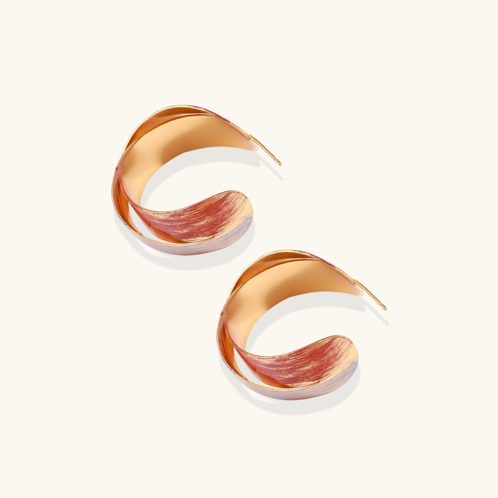 Sculptural gold-plated hoop earrings with diagonal purple and coral enamel stripes in twisted ribbon design